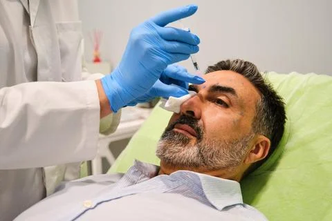 A man is getting Botox for forehead wrinkles by a aesthetic doctor in a clinic. Stock Photos