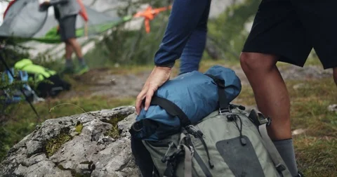 Man getting headlamp from backpack near tent camp. Group of friends summer Stock Footage