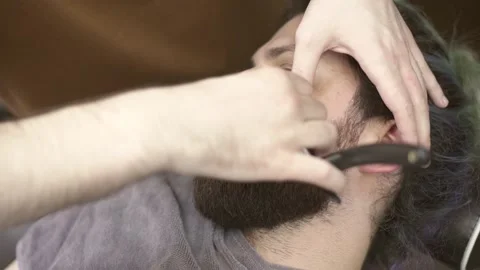 Man getting his beard shaved by professional barber in barber shop Stock Footage 132054424
