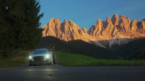 Man getting out of his car at sunset with Dolomites mountain peaks behind Video stock 320458484