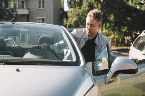 Man getting out of a silver convertible car, holding the steering wheel and d Stock Photos