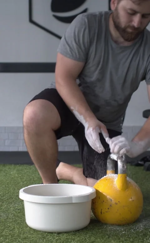Man getting ready by smearing his hands in magnesium to lift a kettlebell Stock Footage 208925763
