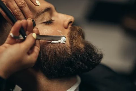 Man getting shaved with straight edge razor by hairdresser at barbershop Stock Photos