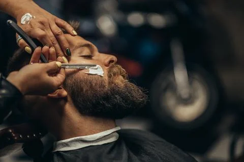Man getting shaved with straight edge razor by hairdresser at barbershop Stock Photos