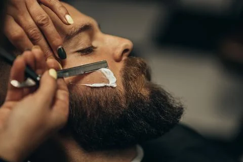 Man getting shaved with straight edge razor by hairdresser at barbershop Stock Photos