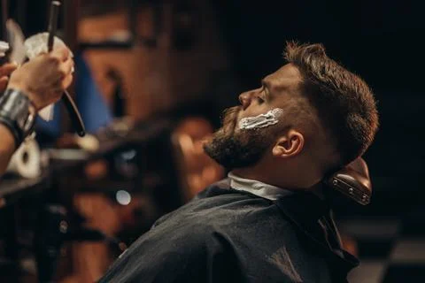 Man getting shaved with straight edge razor by hairdresser at barbershop Stock Photos