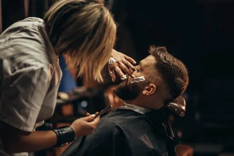 Man getting shaved with straight edge razor by hairdresser at barbershop Stock Photos
