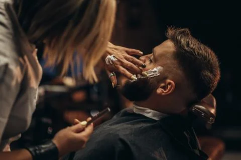 Man getting shaved with straight edge razor by hairdresser at barbershop Stock Photos