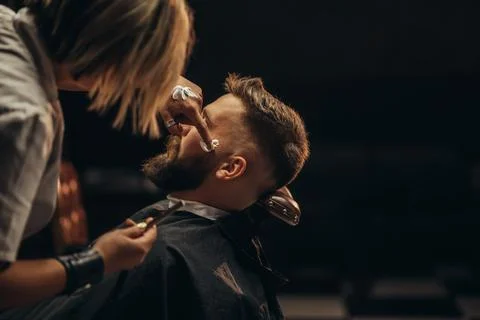 Man getting shaved with straight edge razor by hairdresser at barbershop Stock Photos