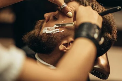 Man getting shaved with straight edge razor by hairdresser at barbershop Stock Photos