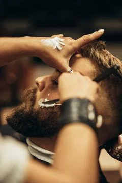 Man getting shaved with straight edge razor by hairdresser at barbershop Stock Photos
