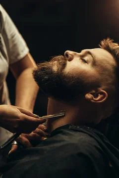 Man getting shaved with straight edge razor by hairdresser at barbershop Stock Photos