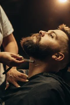 Man getting shaved with straight edge razor by hairdresser at barbershop Stock Photos