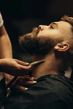 Man getting shaved with straight edge razor by hairdresser at barbershop Stock Photos