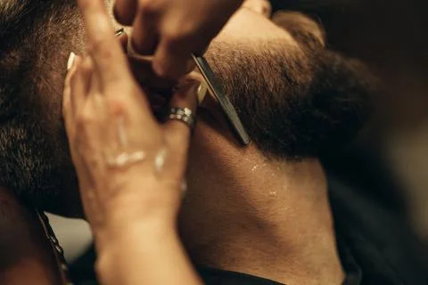 Man getting shaved with straight edge razor by hairdresser at barbershop Stock Photos