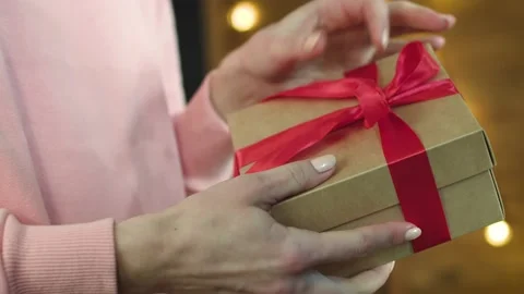 A man gives a gift with a red bow to a woman, hands start to open a present Stock Footage 147036967