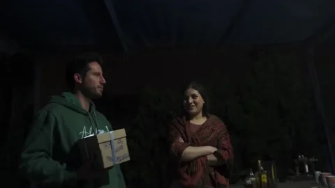 A man giving a box present wrapped with a bow to his friend at a party at night Stock Footage 170019620