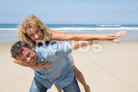 Man giving his pretty girlfriend a piggy back at beach Stock Photos