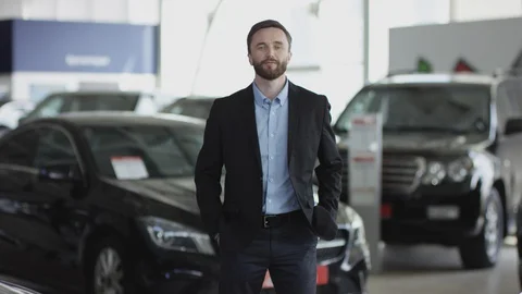 Man is giving thumb-up and posing in car dealership. He is standing between new Stock Footage 129684630