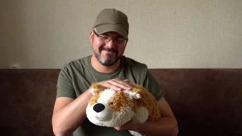 A man in glasses and a baseball cap pets a toy dog 4K Video stock 274402191
