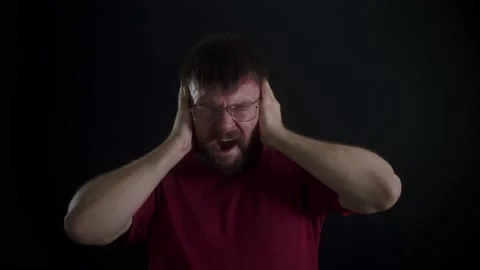 A man with glasses and a beard covers his ears on a black background. Stockbeeldmateriaal 169667670