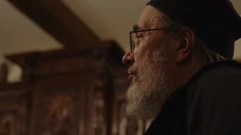 A man with glasses and a beard is having a dialog in a dark room. A priest is Stock Footage 253556917