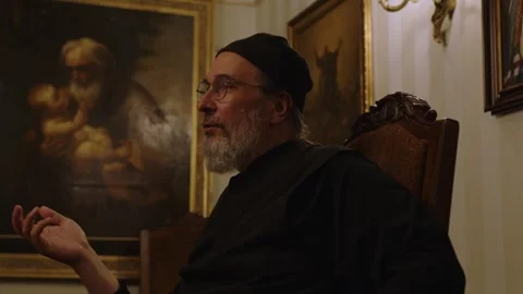 A man with glasses and a beard is having a dialog in a dark room. A priest is Stock Footage 254696721