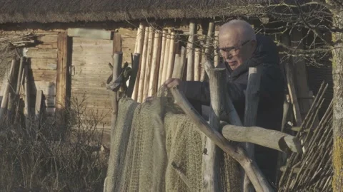 Man in glasses and jacket untangles fishnet on ancient fence Stock Footage 146324969