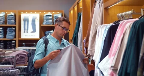 Man glasses, backpack, selects beige sweater, epitome style. Examines it Stock Footage 275085055