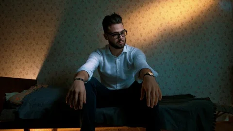 A man with glasses with a beard sits on the couch in a small family depressed Stock Footage 128746965