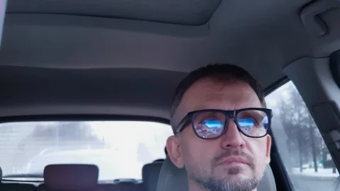 Man with glasses behind steering wheel looks at camera,smiles, shows two fingers Stock Footage 124307243