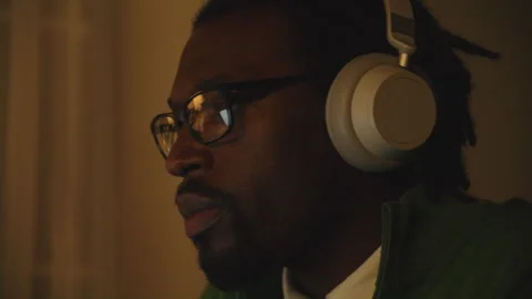 Man with glasses enjoying music while wearing headphones in a dim environment Stock Footage 312584161