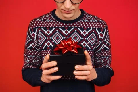 A man in glasses with a gift box in his hands is looking at her, against a re Stock-Fotos
