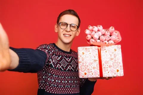 A man in glasses, with a gift in his hands and a bouquet of flowers takes pic Stock Photos