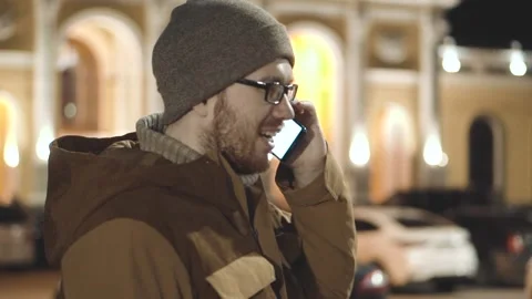 A man with glasses in a happy evening talks on the phone and laughs Stock Footage 231259715