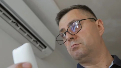 A man with glasses holding a remote control and turning on the air conditioning Stock Footage 109347709