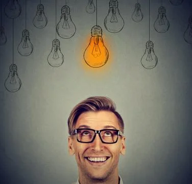 Man in glasses looking up at bright idea light bulb above head Stock Photos