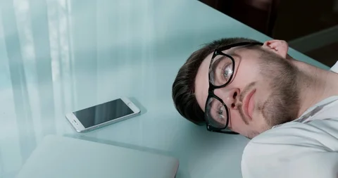 Man in glasses lying on the table with laptop and smartphone. He closes his eyes Stock Footage 120512256