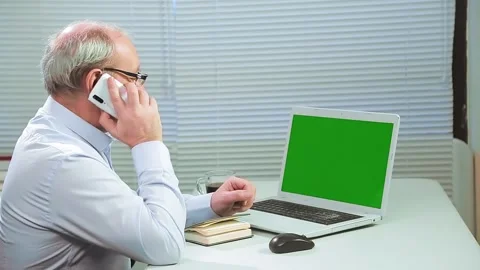 A man in glasses in an office with blinds at a computer works with a green Stock Footage 146805162