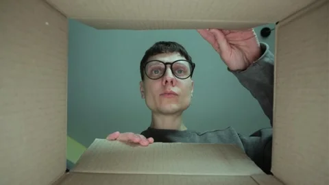 Man in glasses opens a cardboard box, looking inside with a focused expression Stock Footage 303342249