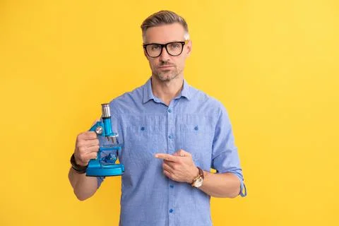 Man in glasses pointing finger on microscope on yellow background, science Foto stock