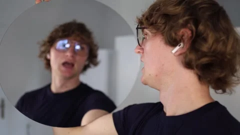 Man with glasses puffs his cheeks and stares into the mirror with a tense expres Video stock 312981803