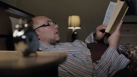 A man in glasses reads a book before going to bed leafing through the page Stock Footage 84740933