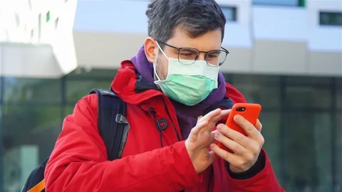 Man in glasses red jacket and respiratory mask on the street and scrolling news Stock Footage 129939176