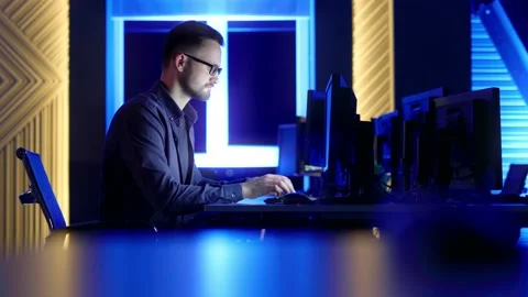 A man with glasses sits and thinks, typing on a computer in the office at night. Video stock 198057917