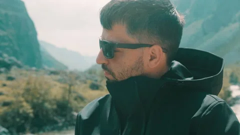 A man with glasses sits on the edge of a cliff wearing a black anorak. Katu Stock Footage 165967249