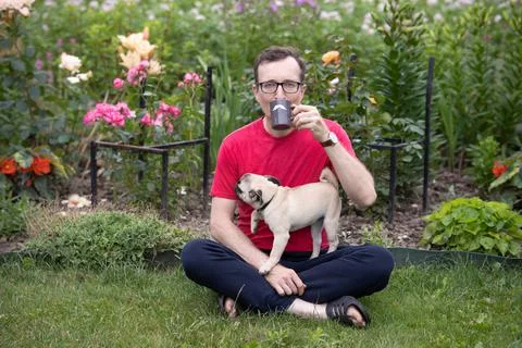 A man with glasses sits on a lawn in a blooming garden and drinks tea from a  Stock Photos
