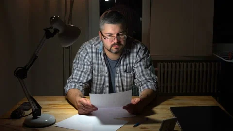 A man with glasses sits at a table and reads 4K Stock Footage 130149267