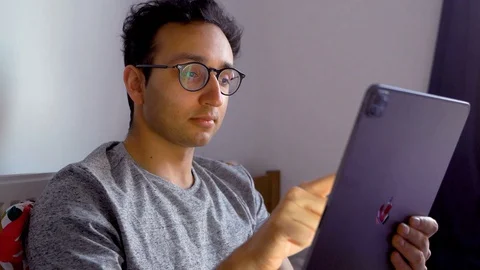 Man with glasses sitting in bed with iPad Pro, scrolling tablet, reading Stock-Footage 129153704