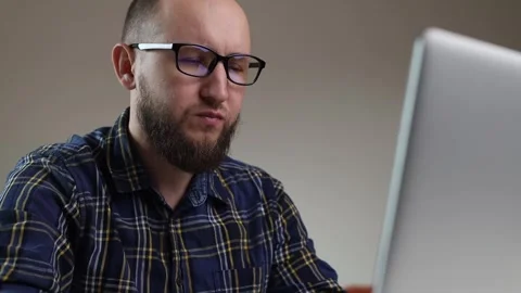 Man with glasses sitting at a table with a laptop Stock Footage 243372024